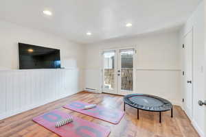 Workout area featuring french doors, wood finished floors, a wainscoted wall, and a baseboard radiator