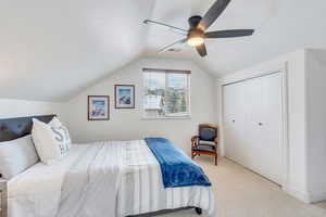 Carpeted bedroom featuring a closet, lofted ceiling, visible vents, and a ceiling fan
