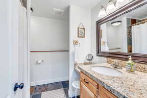 Bathroom featuring a wainscoted wall, baseboards, stone finish flooring, wooden walls, and vanity