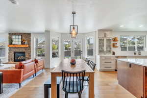 Dining space featuring a healthy amount of sunlight, a stone fireplace, a textured ceiling, and light wood-style flooring