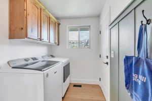 Laundry area with cabinet space, light wood-style flooring, baseboards, visible vents, and independent washer and dryer