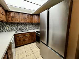 Kitchen with stainless steel appliances, a sink, tasteful backsplash, light countertops, and light tile patterned floors