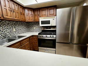 Kitchen featuring a sink, tasteful backsplash, brown cabinets, light countertops, and appliances with stainless steel finishes