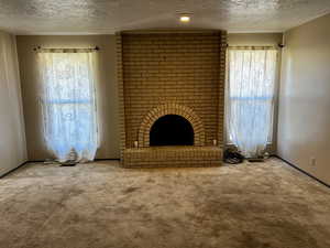 Unfurnished living room featuring a brick fireplace, a textured ceiling, carpet flooring, and baseboards