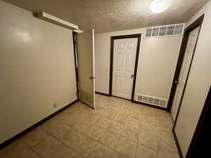 Interior space with light tile patterned flooring, a textured ceiling, visible vents, and baseboards