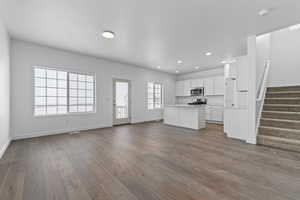 Unfurnished living room with dark wood-type flooring, stairway, baseboards, and recessed lighting