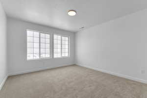 Empty room with carpet, a textured ceiling, baseboards, and visible vents