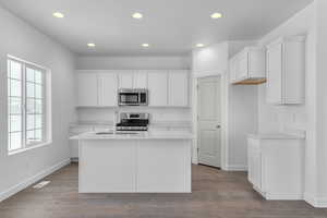 Kitchen with baseboards, recessed lighting, appliances with stainless steel finishes, and a center island with sink