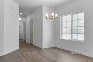 Unfurnished dining area with wood-type flooring, baseboards, and a notable chandelier
