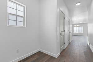 Corridor featuring dark wood-style flooring, baseboards, and a notable chandelier