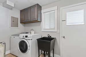 Laundry area with a sink, electric panel, baseboards, washer and dryer, and cabinet space
