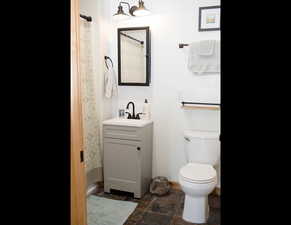 guest Full bath with toilet, baseboards, stone finish flooring, a shower with shower curtain, and vanity
