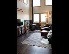 Living room featuring a high ceiling, a wood stove, and wood finished floors