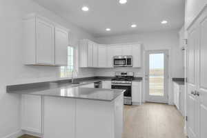 Kitchen featuring stainless steel appliances, a peninsula, a sink, recessed lighting, and white cabinetry