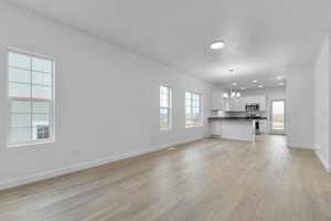 Unfurnished living room featuring recessed lighting, light wood-style flooring, baseboards, and an inviting chandelier
