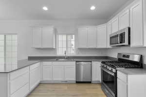 Kitchen featuring stainless steel appliances, a peninsula, a sink, recessed lighting, and white cabinetry