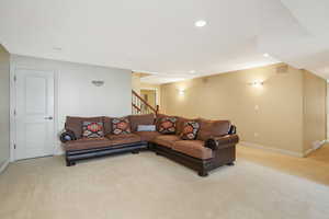 Living area with baseboards, stairs, and light colored carpet