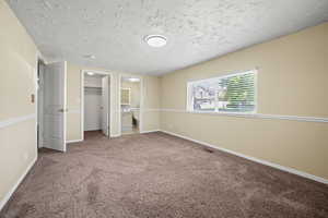Unfurnished bedroom with baseboards, carpet flooring, a textured ceiling, and a walk in closet