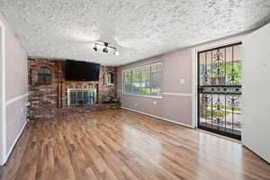 Unfurnished living room with a brick fireplace, a textured ceiling, baseboards, and wood finished floors