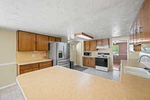 Kitchen with brown cabinets, a sink, baseboards, under cabinet range hood, and stainless steel appliances