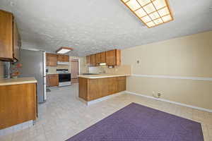 Kitchen featuring light countertops, range with electric cooktop, brown cabinetry, a peninsula, and under cabinet range hood