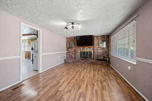 Unfurnished living room with a textured ceiling, a brick fireplace, wood finished floors, and visible vents