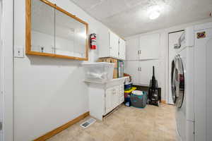 Clothes washing area with cabinet space, a textured ceiling, baseboards, washer / dryer, and visible vents