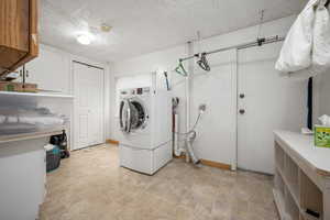 Washroom with baseboards, washer / clothes dryer, stone finish floor, a textured ceiling, and cabinet space