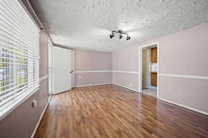 Empty room featuring a textured ceiling, baseboards, and wood finished floors