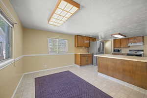 Kitchen featuring light countertops, appliances with stainless steel finishes, baseboards, and brown cabinetry