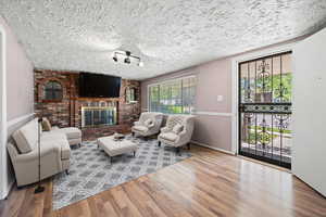 Living area with a textured ceiling, wood finished floors, baseboards, and a brick fireplace
