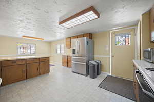 Kitchen featuring light countertops, appliances with stainless steel finishes, baseboards, and brown cabinets