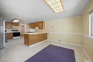 Kitchen with white electric range oven, a sink, freestanding refrigerator, a peninsula, and under cabinet range hood