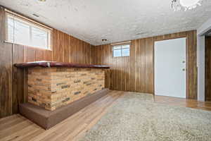 Bar featuring visible vents, a textured ceiling, light wood finished floors, and wooden walls