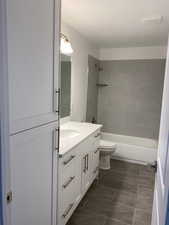 Bathroom with a textured ceiling, toilet, vanity, and  shower combination
