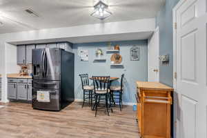 Kitchen with a textured ceiling, visible vents, light wood-style floors, gray cabinetry, and stainless steel refrigerator with ice dispenser