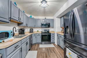Kitchen featuring a sink, gray cabinetry, a textured ceiling, appliances with stainless steel finishes, and dark wood-style flooring