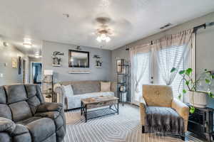 Carpeted living area featuring visible vents, a textured ceiling, and ceiling fan