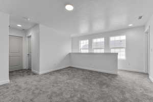 Carpeted spare room with baseboards, a textured ceiling, and visible vents