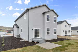 Back of house with stucco siding, central AC unit, and a yard