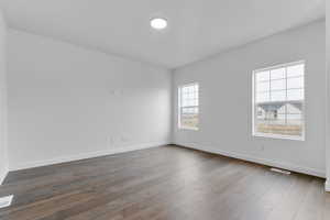 Empty room with baseboards, dark wood-type flooring, and visible vents