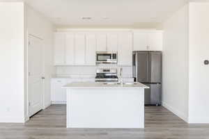 Kitchen with white cabinetry, baseboards, appliances with stainless steel finishes, and a kitchen island with sink