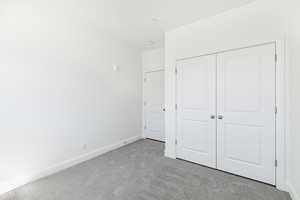 Unfurnished bedroom featuring light colored carpet, baseboards, and a closet