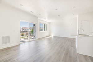 Unfurnished living room featuring visible vents, light wood finished floors, baseboards, and a sink