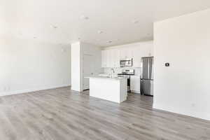 Kitchen with light wood-style floors, a center island with sink, appliances with stainless steel finishes, and open floor plan
