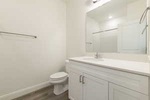 Bathroom featuring wood finished floors, vanity, a shower, baseboards, and toilet