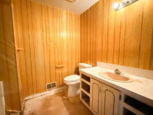 Bathroom featuring wood walls, visible vents, toilet, vanity, and concrete floors