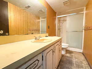 Full bathroom with a textured ceiling, toilet, a stall shower, unfinished concrete flooring, and vanity