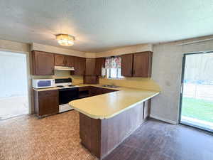 Kitchen with range with electric stovetop, white microwave, light countertops, a peninsula, and under cabinet range hood