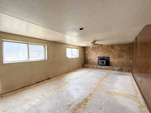 Unfurnished living room featuring a textured ceiling, a wood stove, and a ceiling fan